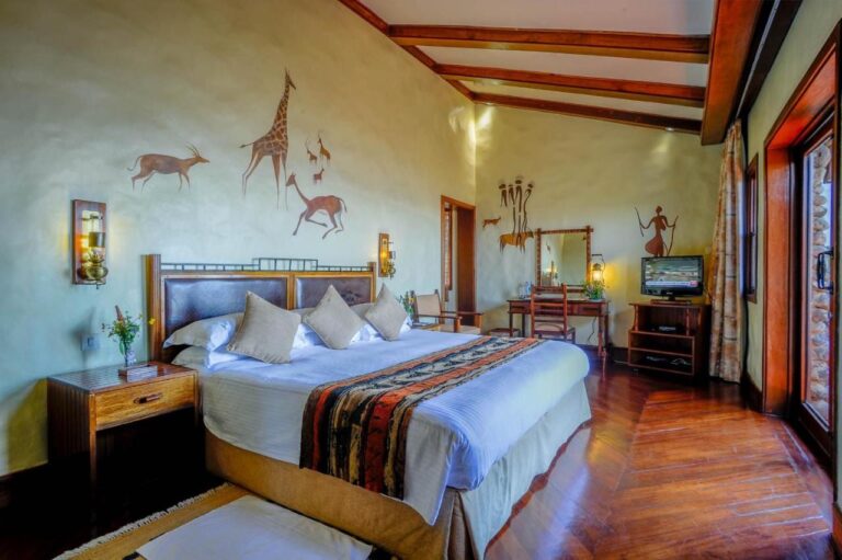 Une chambre avec un grand lit, un bureau, une télévision et une girafe peinte au mur