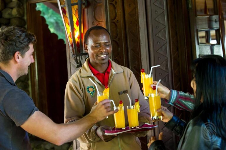 Un employé du Ngorongoro Serena Safari Lodge tend un plateau de jus de fruits à deux voyageurs
