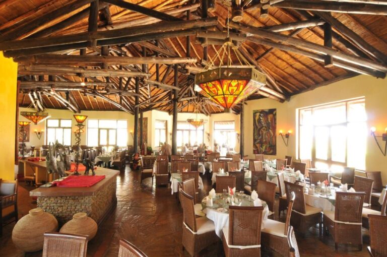 La salle du restaurant sous une charpente de rondins, avec des lustres en vitrail et des tables nappées de blanc