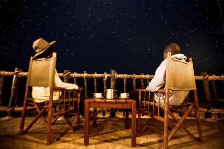 Deux personnes assises dans des fauteuils de toile sur la terrasse, deux tasses sur la table, sous un ciel étoilé