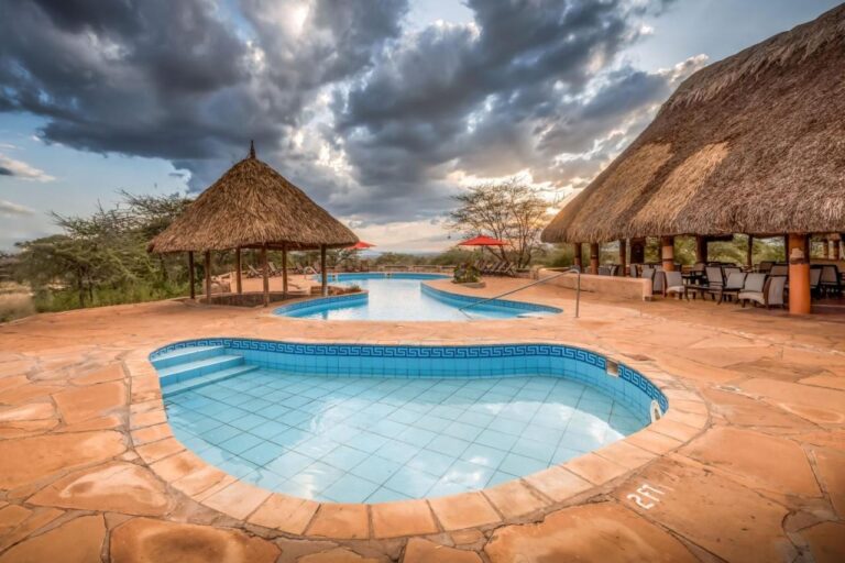 Un petit bassin carrelé au premier plan et la grande piscine du Samburu Sopa Lodge, entre une paillote et une terrasse au toit de chaume