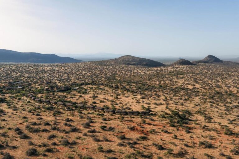 Le lodge vu d'en haut, ses bungalows au toit de chaume alignés dans la brousse sèche, devant des collines