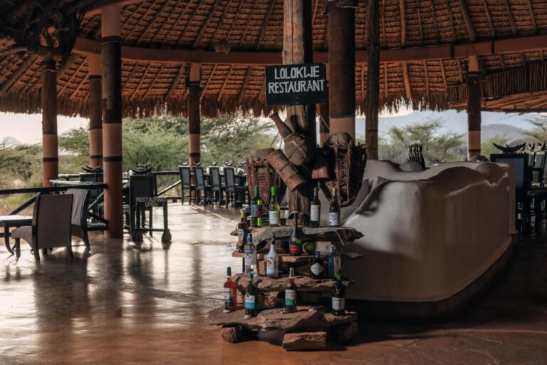 L'entrée du restaurant Lolokwe, avec des bouteilles de vin posées sur des pierres, sous un grand toit de chaume