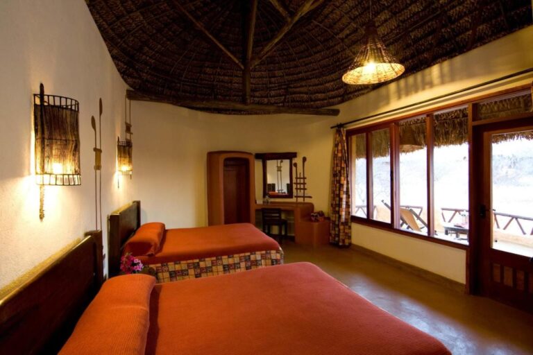 Une chambre à deux lits aux couvre-lits orange, avec de grandes fenêtres donnant sur une terrasse