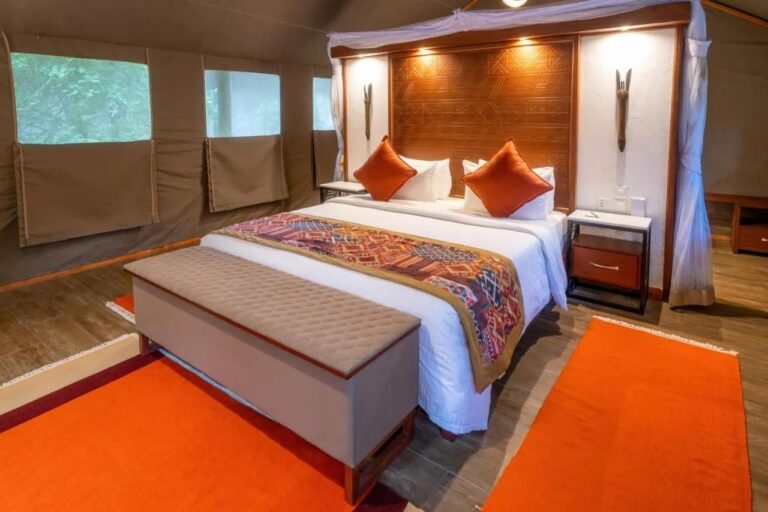 Le lit d'une tente vu de biais, avec sa tête de lit en bois et ses tapis orange