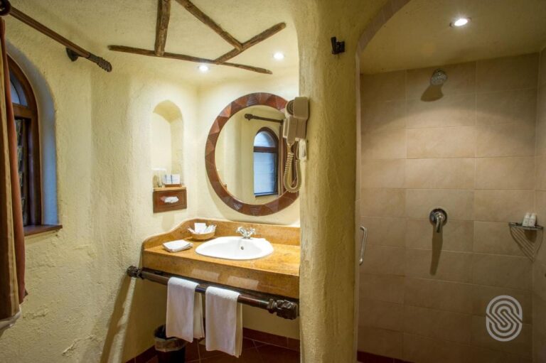 Une salle de bains aux murs crépis, avec un lavabo sous un miroir rond et une grande douche carrelée