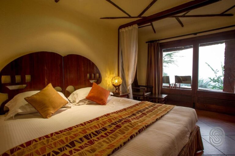 Un grand lit aux draps blancs et aux coussins orange, sous une tête de lit en bois arrondie