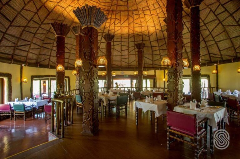 La salle du restaurant sous sa coupole, ses colonnes de bois sculptées de personnages et ses tables nappées de blanc