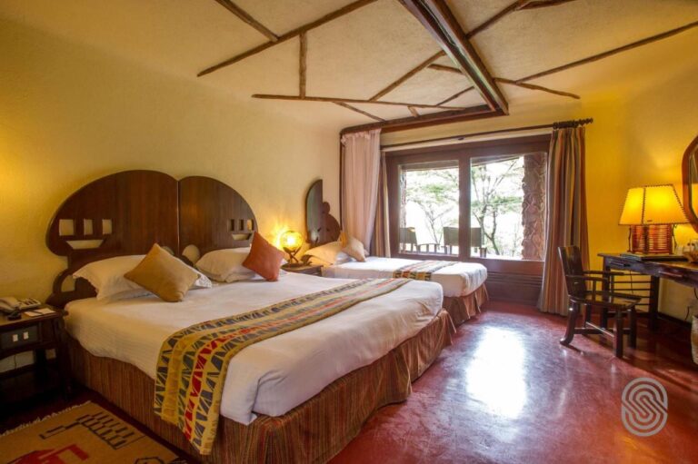 Une chambre avec un grand lit et un lit simple aux têtes de lit en bois découpé, et un bureau près de la fenêtre