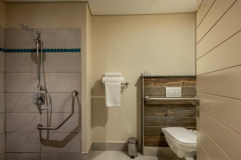 Une salle de bains avec douche de plain-pied, barres d'appui et toilettes suspendues