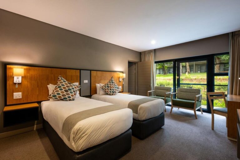 Une chambre à deux lits, avec deux fauteuils devant la baie vitrée