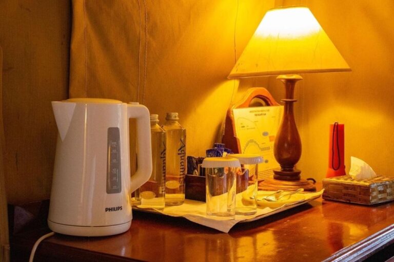 Une bouilloire, des bouteilles d'eau et des verres sur un bureau, sous une lampe