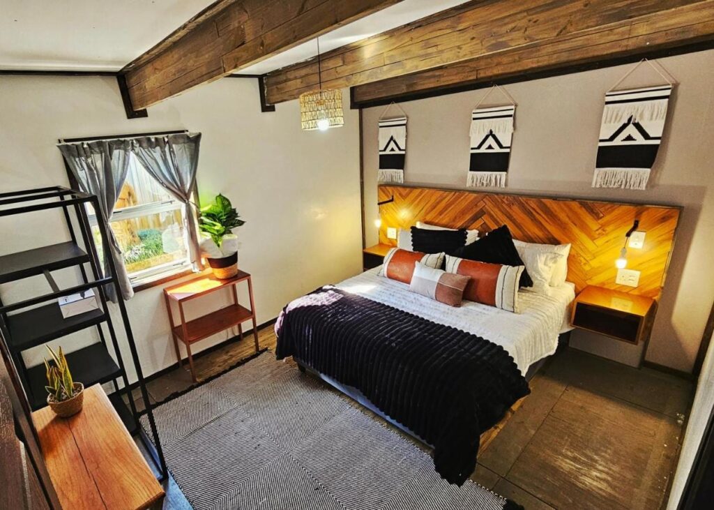 Une chambre de The Elements avec un grand lit, une tête de lit en bois à chevrons et trois tentures noir et blanc, sous des poutres apparentes