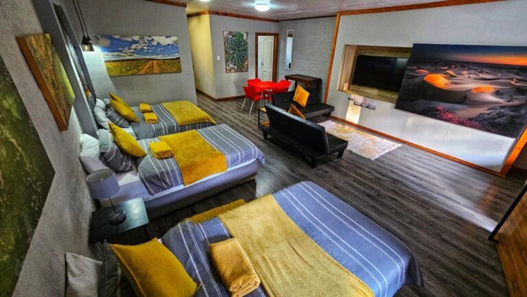 Un grand logement avec trois lits aux plaids jaunes, un canapé noir, une table rouge et de grandes photos de paysages aux murs