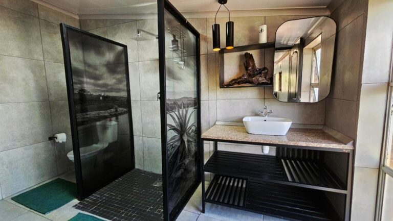 Une salle de bains avec une douche derrière des parois vitrées ornées de photos en noir et blanc, et une vasque posée sur un meuble noir