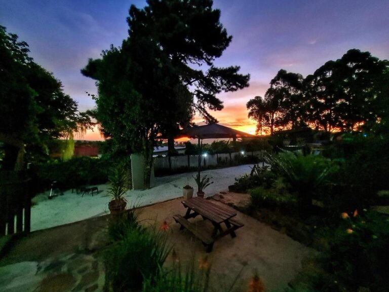 Le jardin au coucher du soleil, avec une table de pique-nique sous de grands arbres et un ciel orangé
