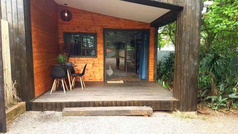 La terrasse en bois d'un chalet, avec une table et deux chaises noires devant une porte vitrée coulissante