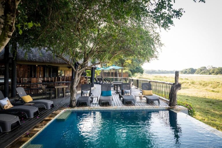 La piscine de l'Umkumbe Safari Lodge et sa terrasse en bois, au-dessus de la berge herbeuse de la rivière
