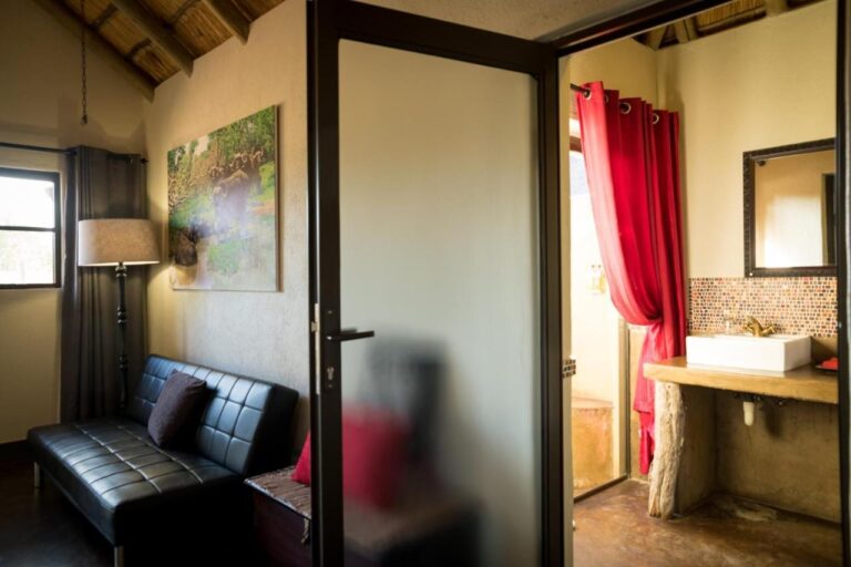 Le coin salon d'une chambre, avec un canapé en cuir noir, et la salle de bains derrière une porte vitrée