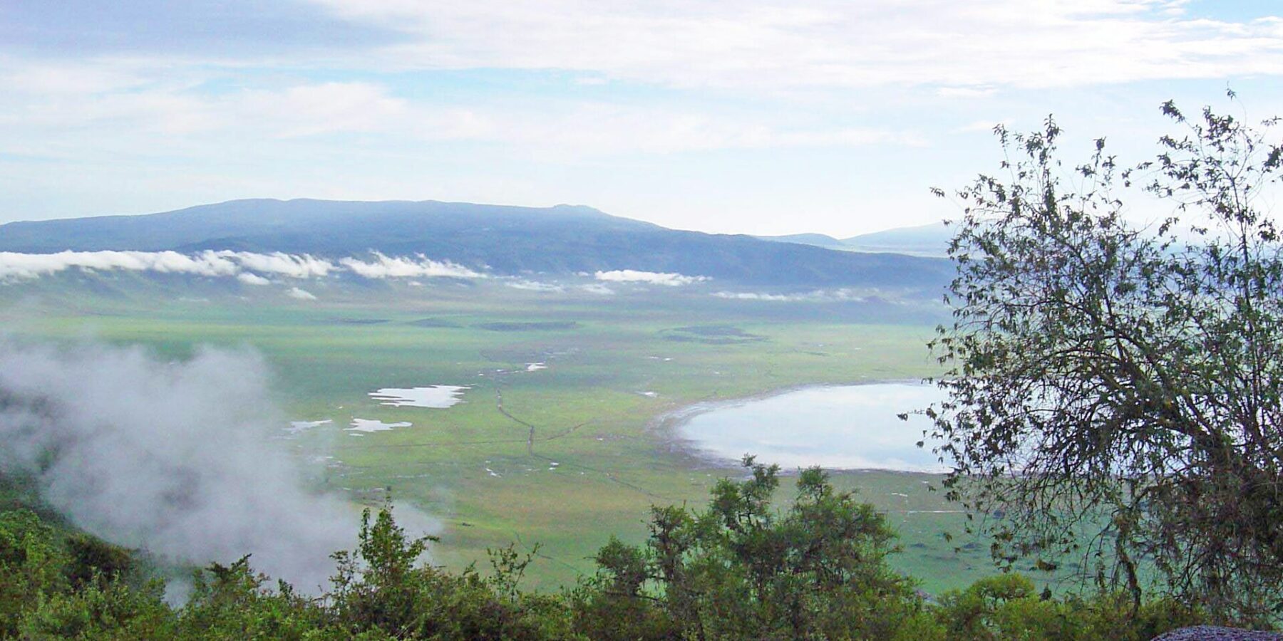 Le fond vert du cratère vu depuis le rebord, avec le lac Magadi et des nuages accrochés aux parois